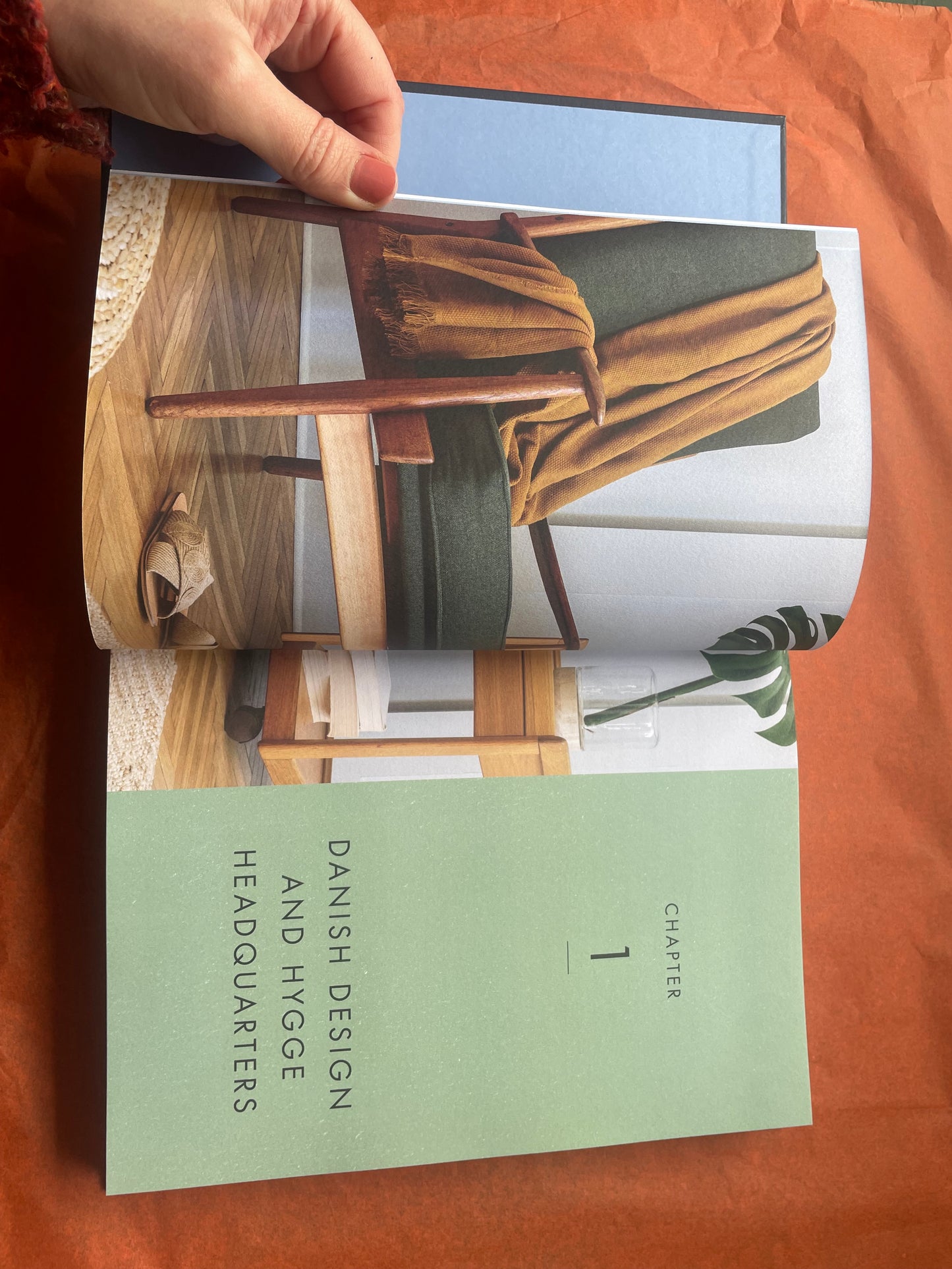 This shows a hand flicking through the book open on a chapter that reads Danish Design and Hygge headquarters.