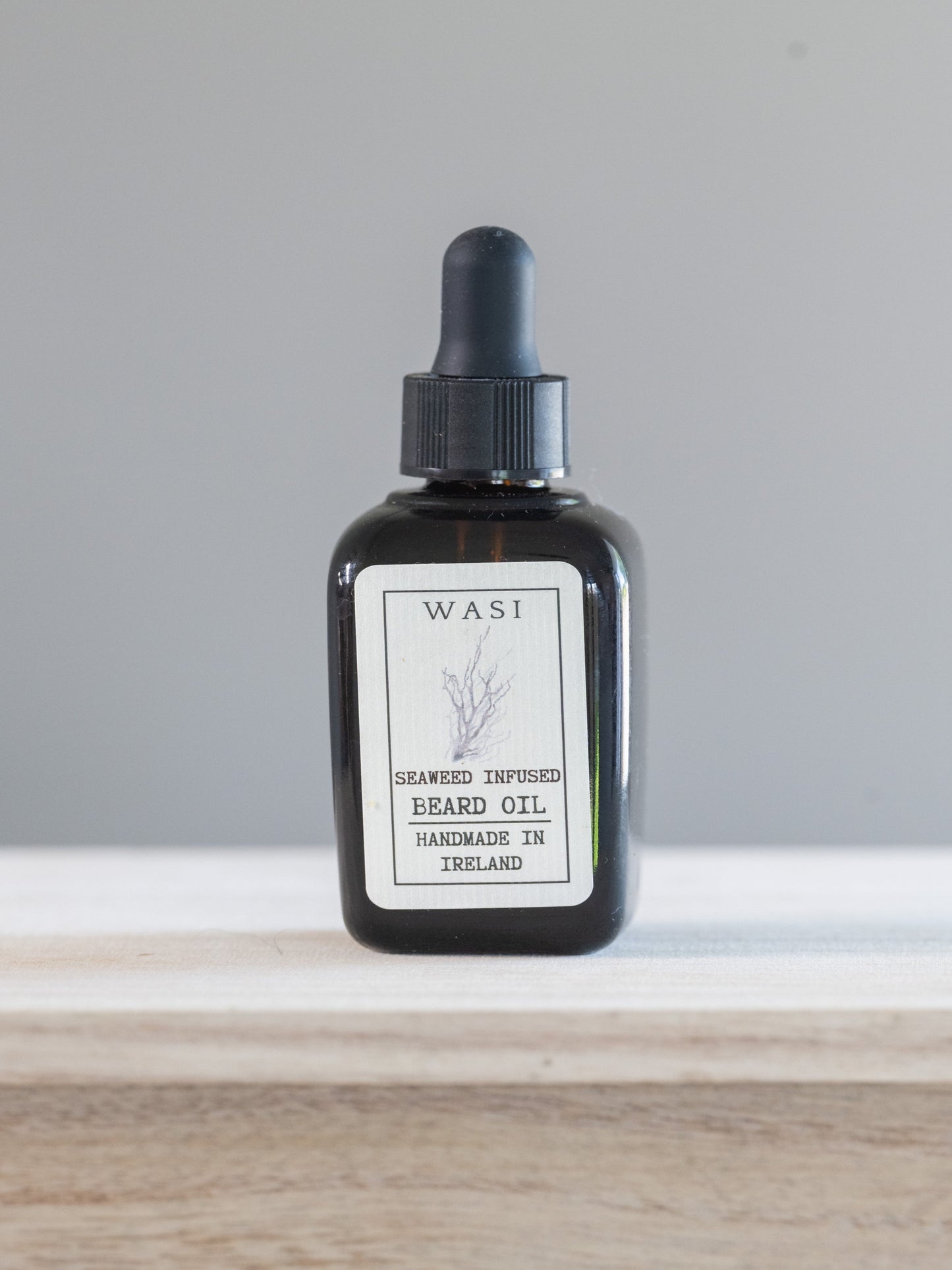 Black bottle of WASI beard oil with a dropper on a white surface.