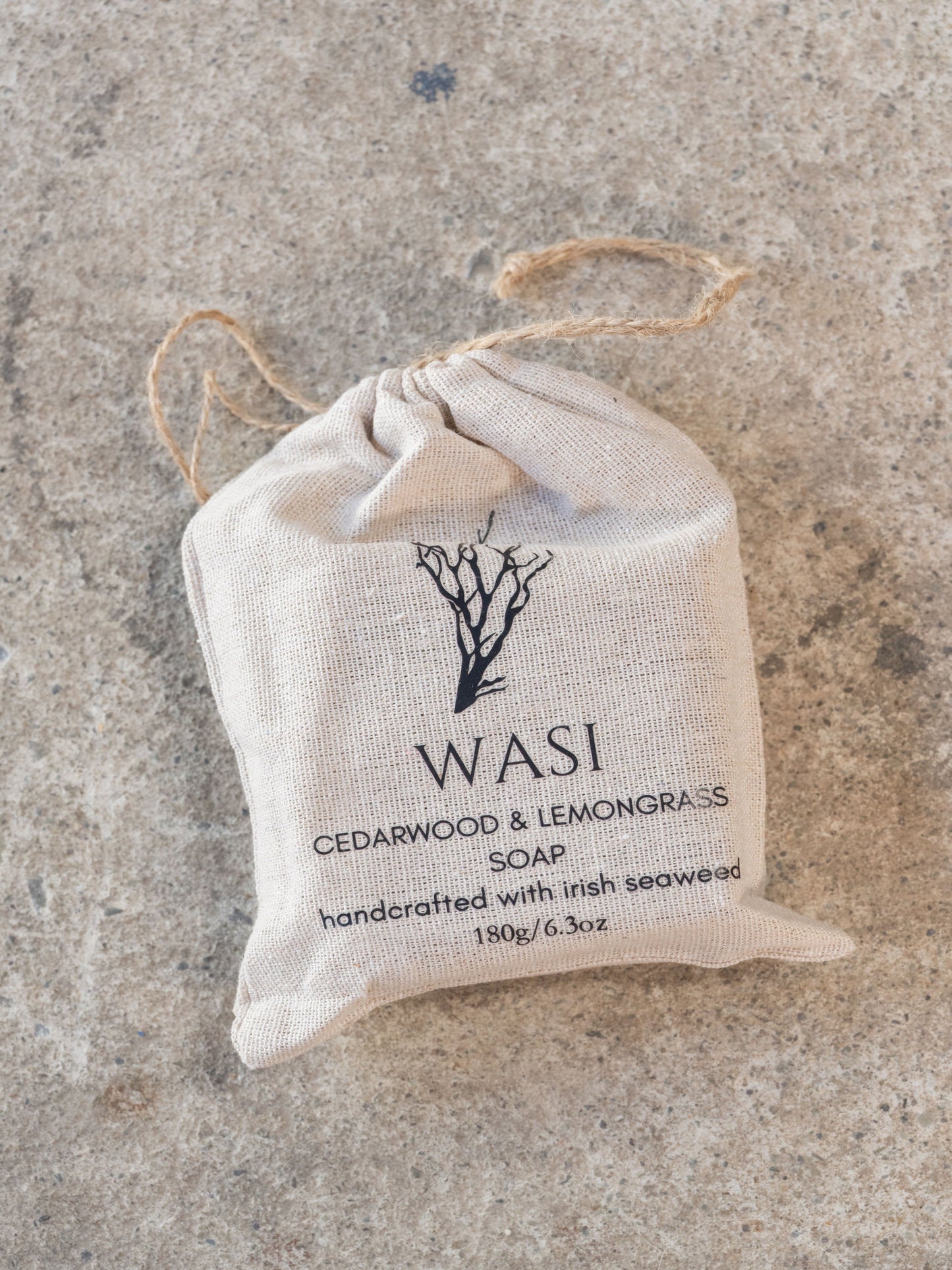 WASI cedarwood & lemongrass soap in a drawstring bag on a concrete surface