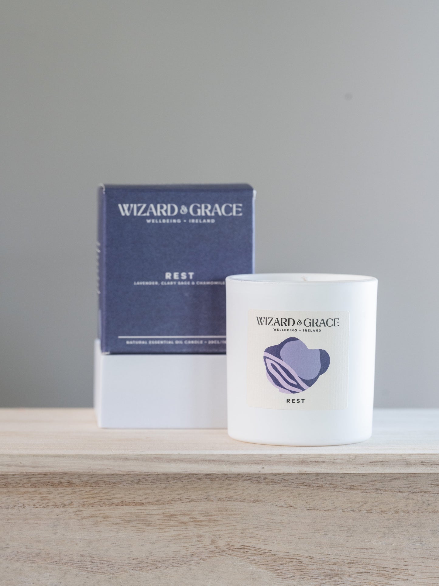 Candle and packaging with 'Wizard of Grace' branding on a wooden surface.
