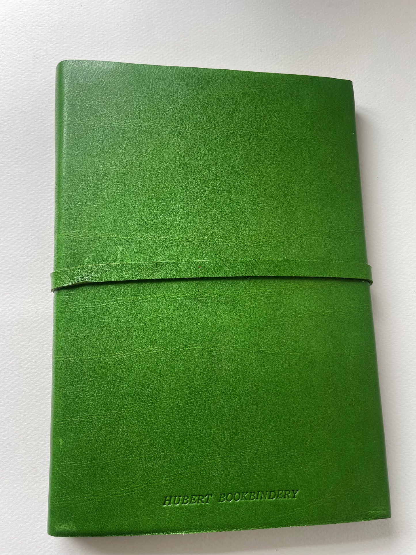 The back of a green leather bound note book that is lined, it's handmade with the imprint Hubert Bookbindery on the bottom.
