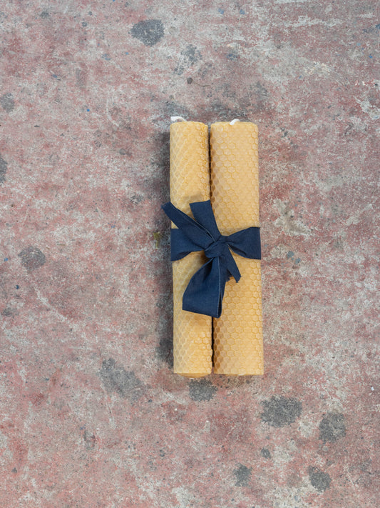 Set of two yellow beeswax candles tied with a navy bow.