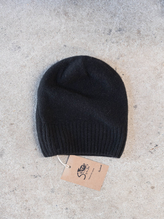 Black knit beanie with a tag on a light gray surface