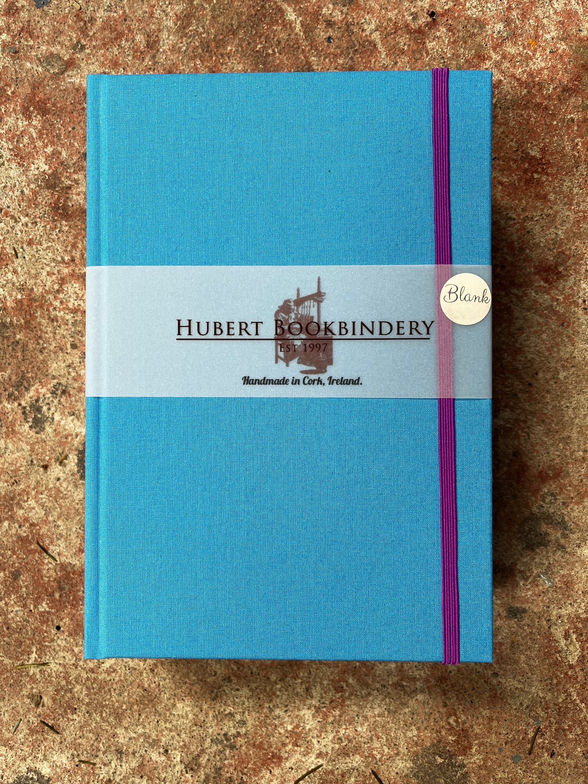 Blue notebook with Hubert Bookbindery branding on a textured surface
