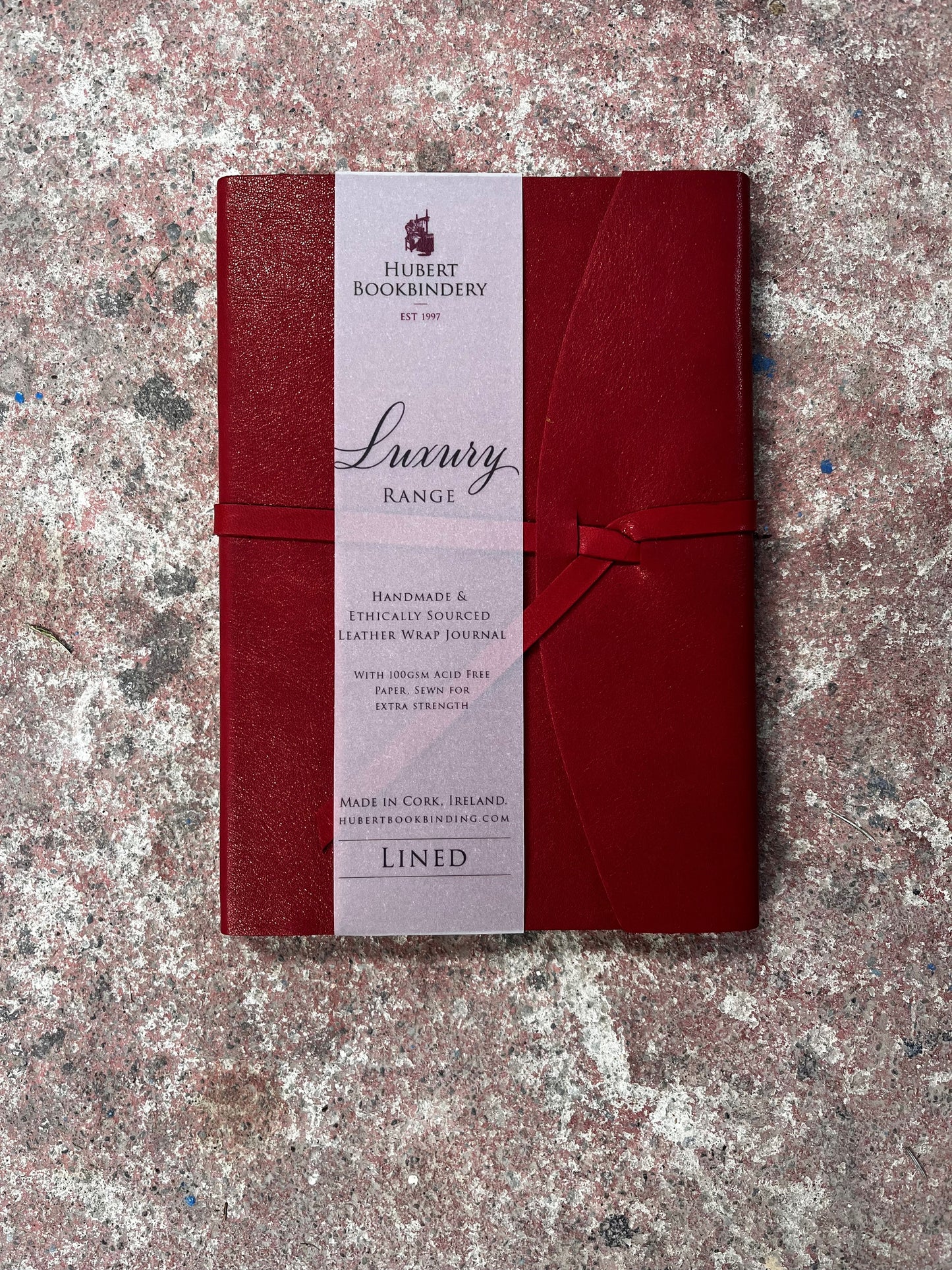 Red leather-bound book with Hubert Bookbindery label on a textured surface