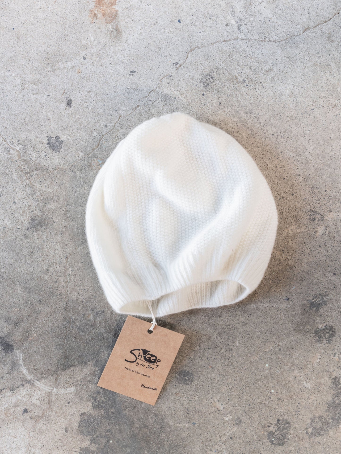 White knit beanie on a textured gray surface with a tag attached.