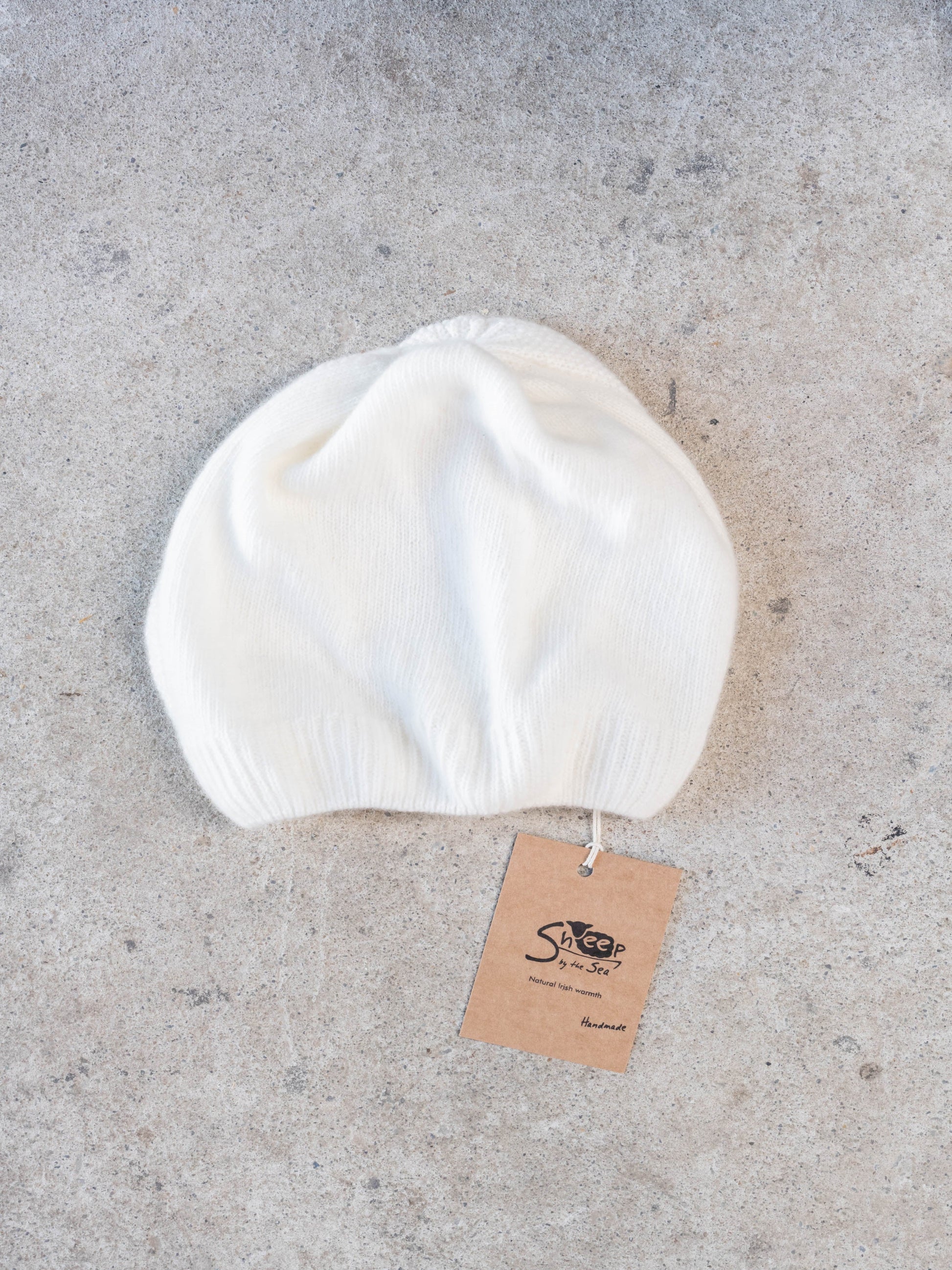 White beanie on a gray concrete surface with a brand tag attached.
