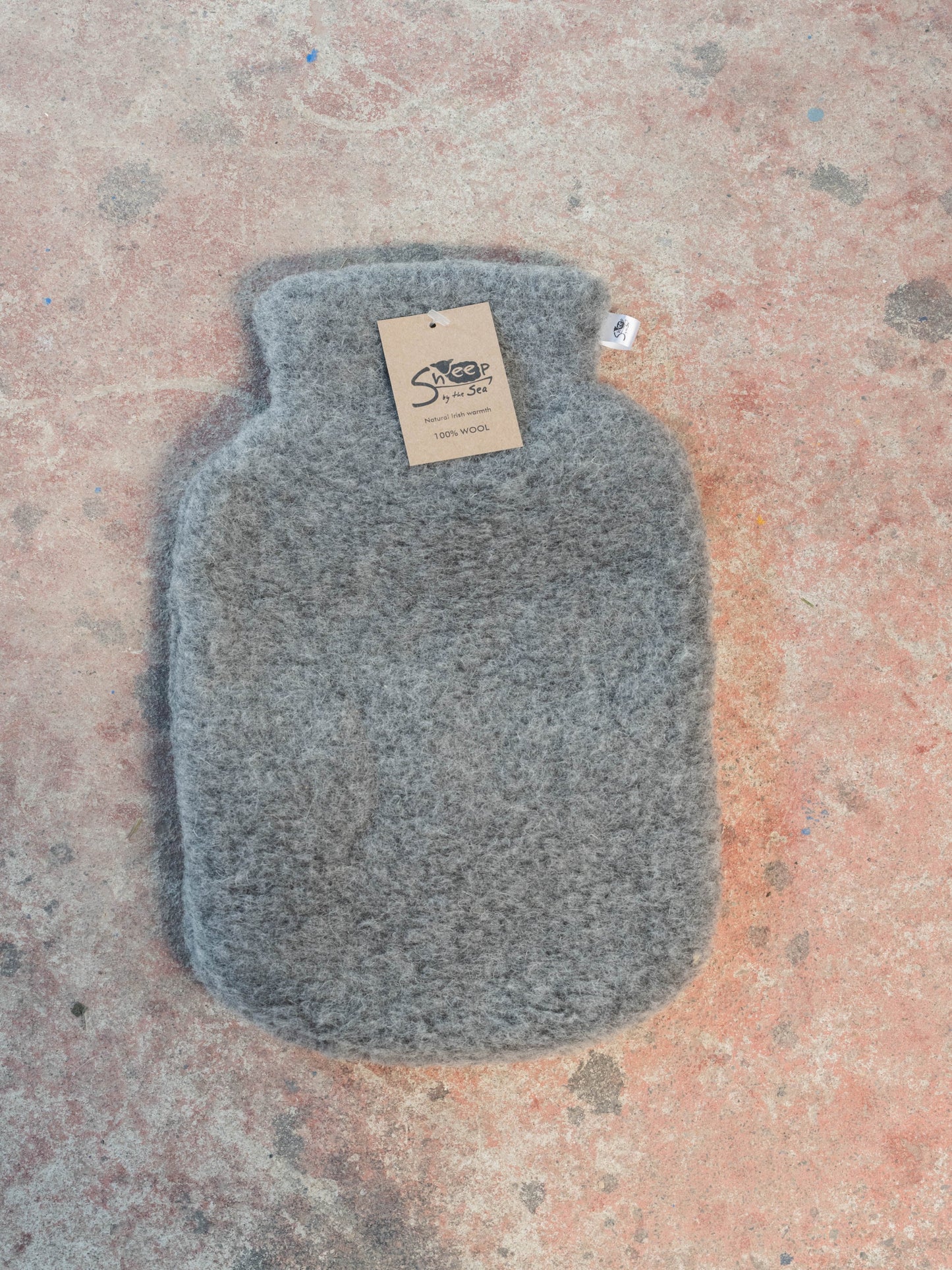 Gray hot water bottle with a tag on a textured surface.
