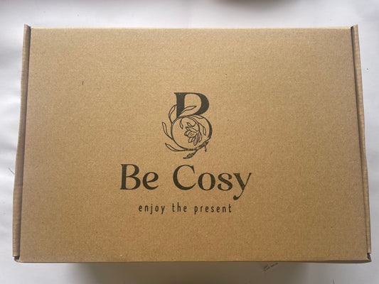 This is a picture of a large brown box with the words 'Be Cosy' enjoy the present n the front. There is a large B on top of the words Be Cosy with a hand drawn logo with jasmine flowers coming out of it. 