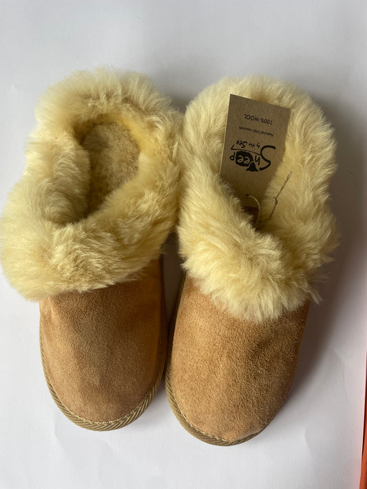 This image depicts tan slippers that are sheep lined with cream wool. They also have the sheep by the sea logo and are made from wool. They look cosy and inviting and owning a pair, I can speak to that! 
