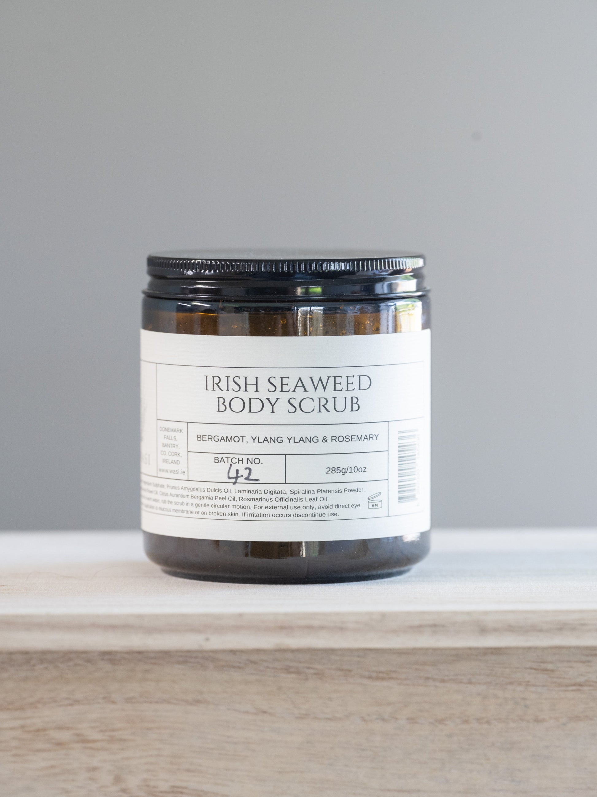 Jar of Irish Seaweed Body Scrub on a white surface with a gray background. This natural seaweed body scrub is infused with nutrient-rich seaweed, this scrub detoxifies while sloughing away dullness, revealing soft, glowing skin beneath. Formulated to compliment our best-selling body oil, this scrub pairs perfectly to lock in hydration, leaving your skin irresistibly smooth and fragrant.