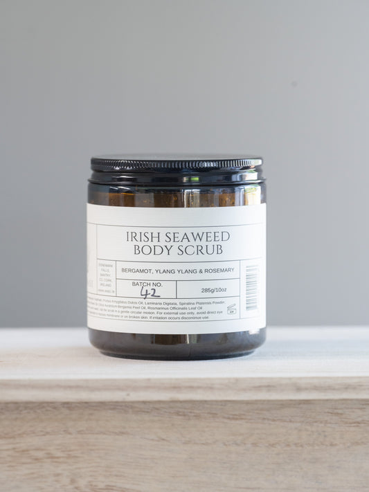 Jar of Irish Seaweed Body Scrub on a white surface with a gray background. This natural seaweed body scrub is infused with nutrient-rich seaweed, this scrub detoxifies while sloughing away dullness, revealing soft, glowing skin beneath. Formulated to compliment our best-selling body oil, this scrub pairs perfectly to lock in hydration, leaving your skin irresistibly smooth and fragrant.