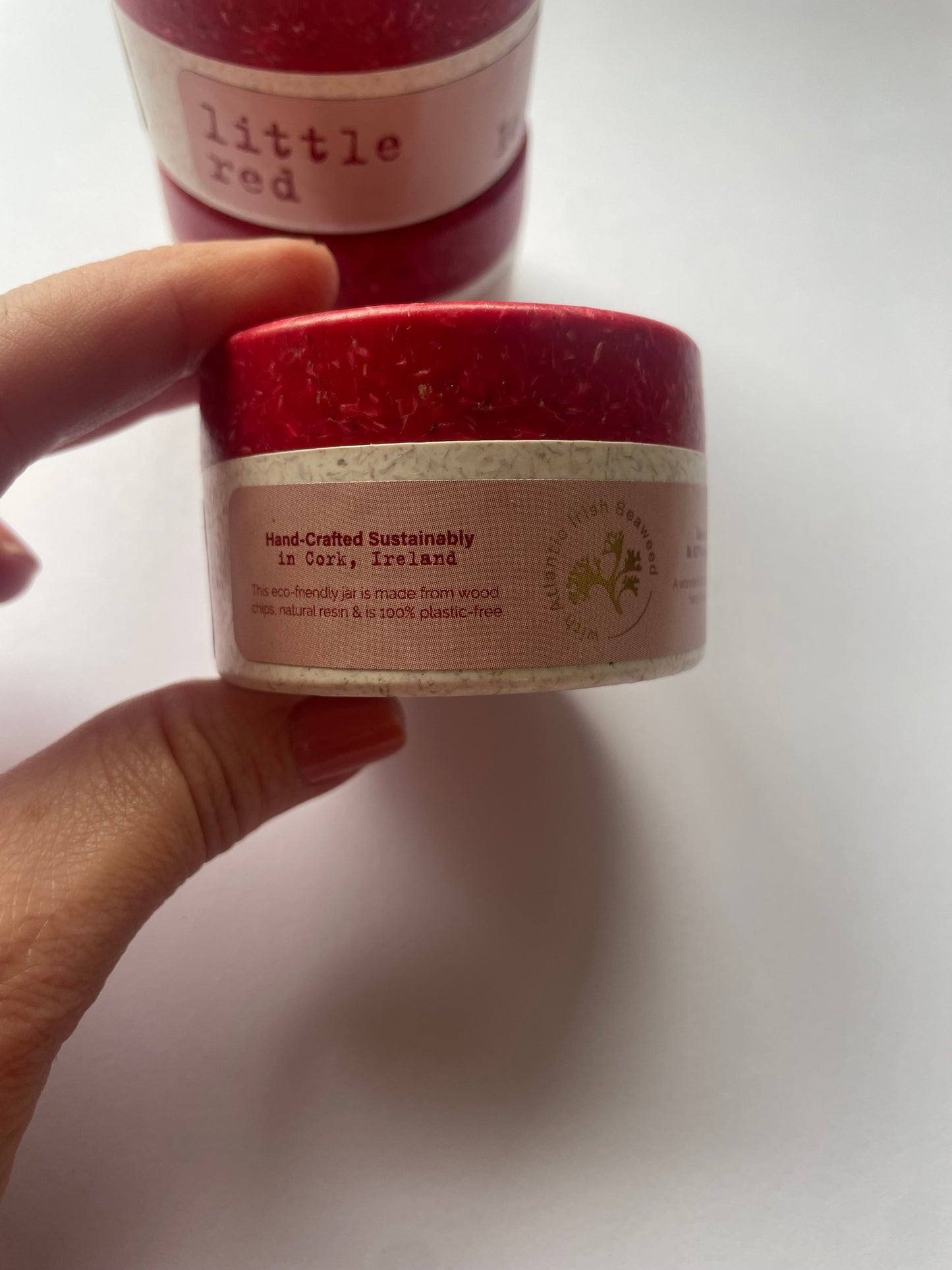This shows two fingers holding a jar of hand cream that reads hand-crafted sustainably. 