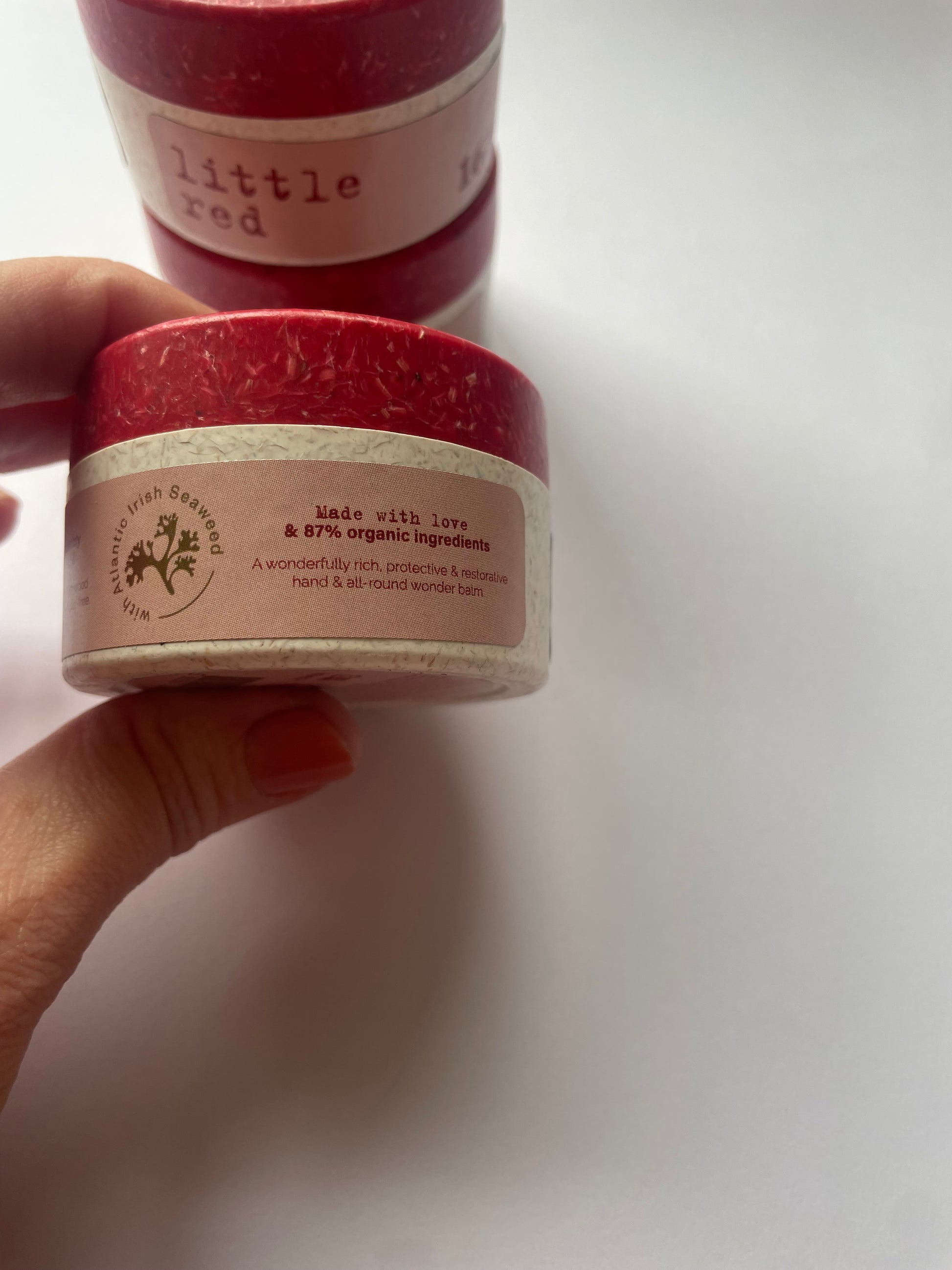 This shows two fingers holding a pot of hand cream with the words made with love and 87% organic ingredients. 