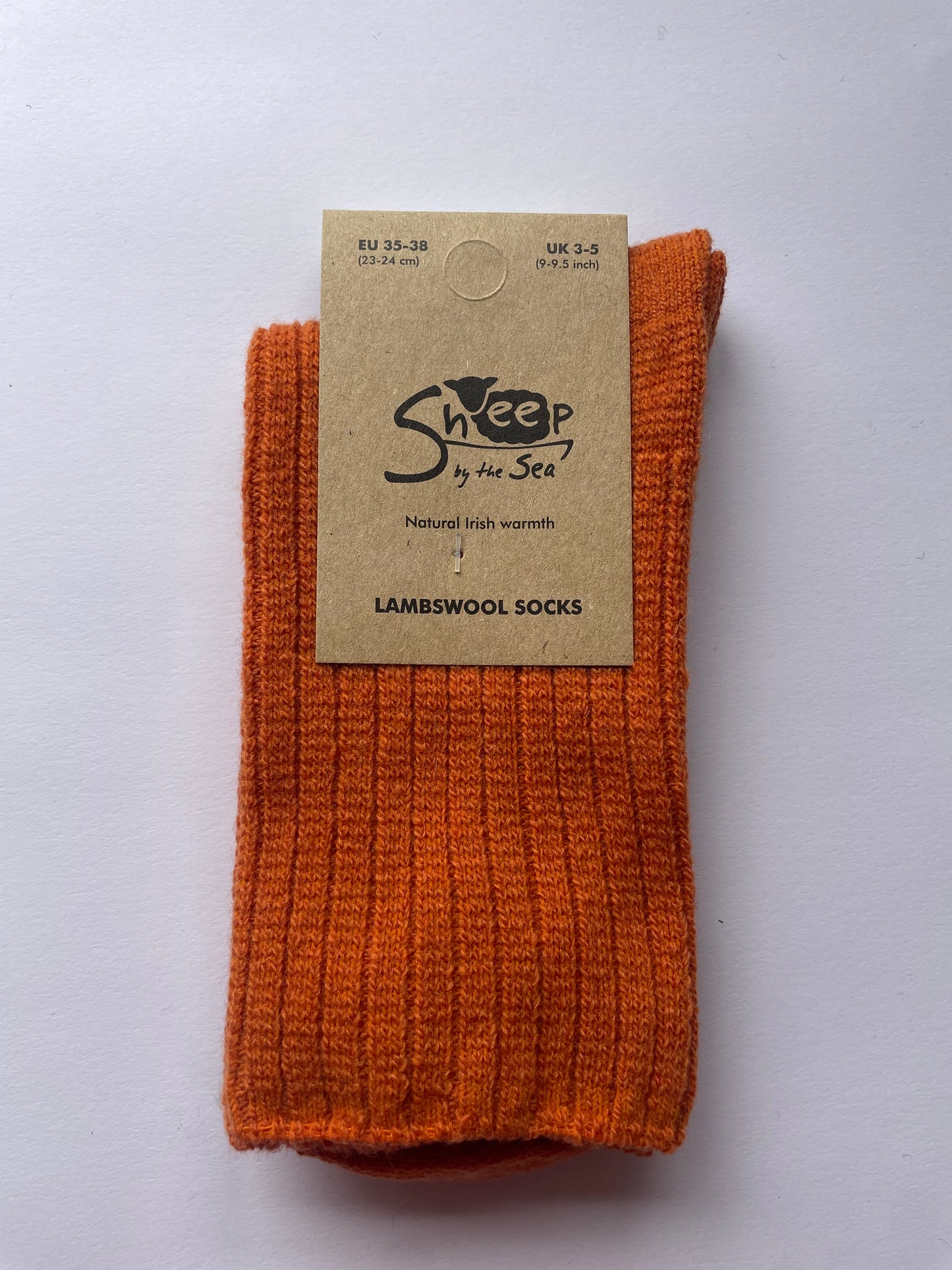 Orange socks with a brown label that says sheep by the sea, natural Irish warmth, lambs wool socks. 