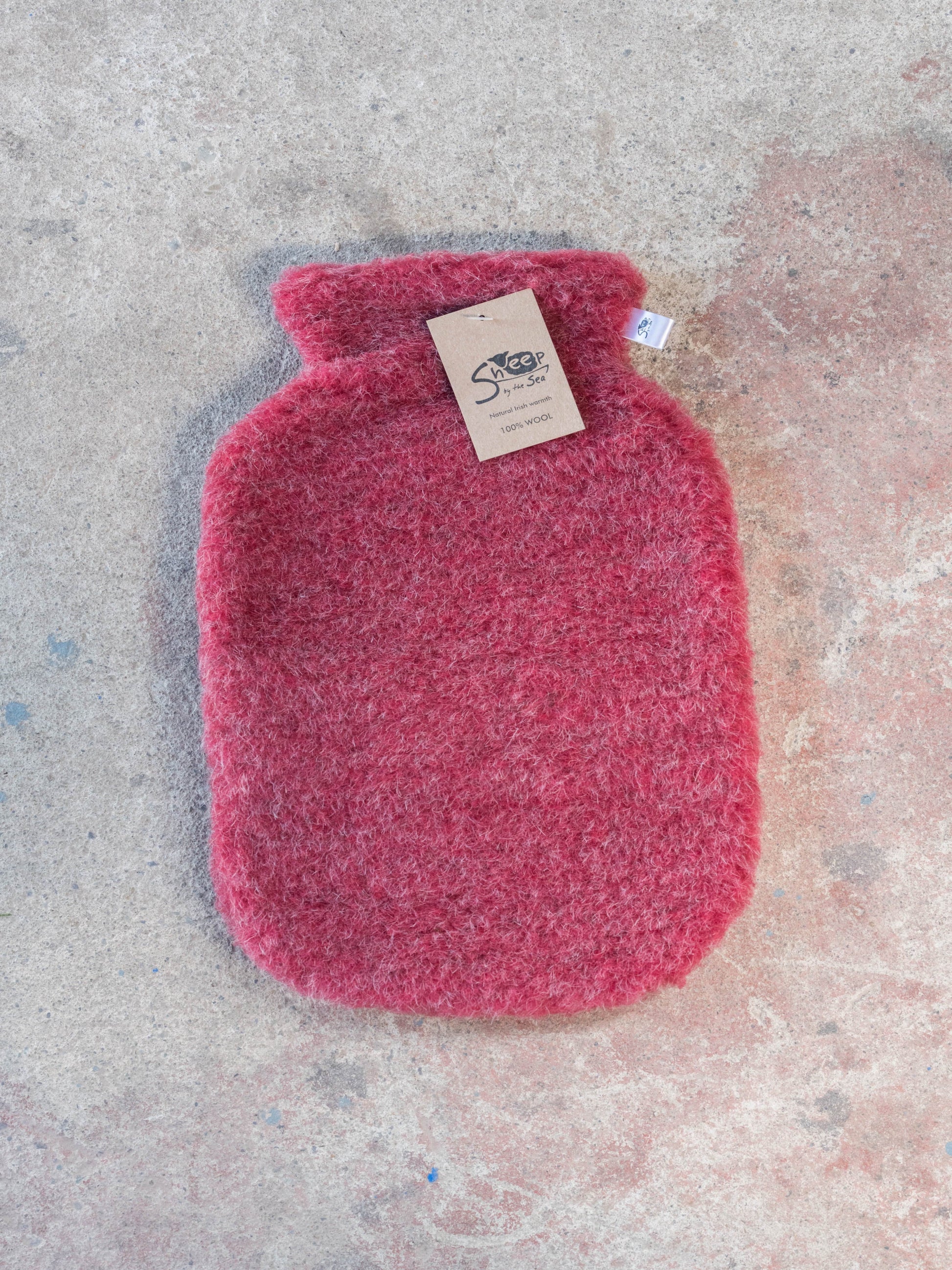 Pink hot water bottle with a label on a textured surface