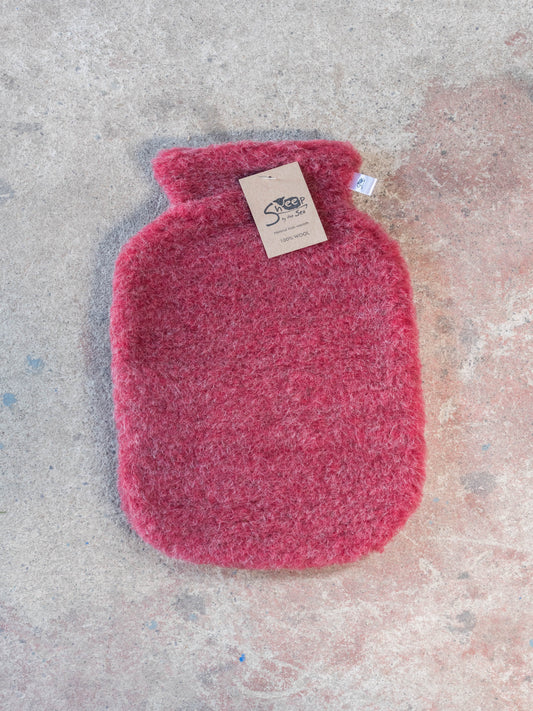 Pink hot water bottle with a label on a textured surface