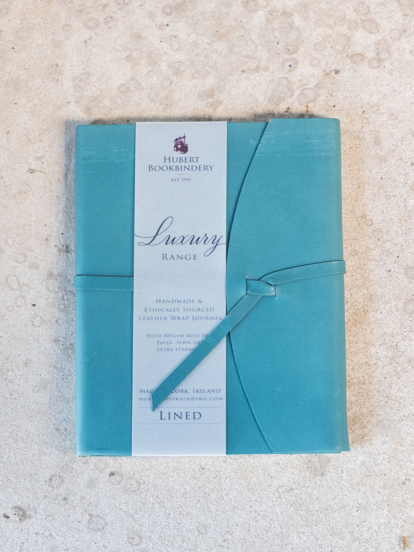 Teal notebook with a ribbon on a textured beige surface