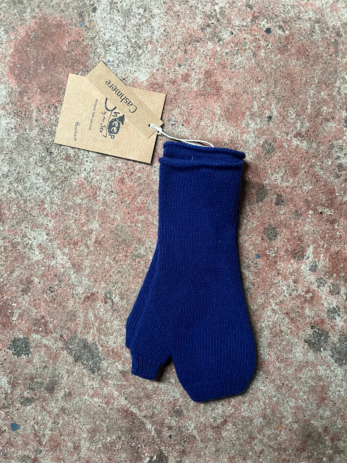 A single dark blue ribbed knit bootie or mitten-style sock with a small paper tag attached, placed on a mottled stone surface.